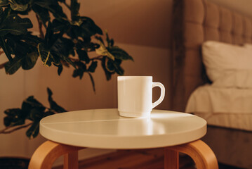 White coffee cup on the table in sunny morning bedroom, mock up.