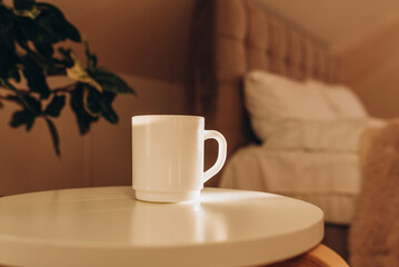White coffee cup on the table in sunny morning bedroom, mock up.