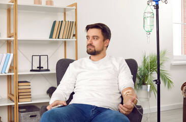 Young man sitting in armchair receiving intravenous treatment. Male patient getting treatment or...