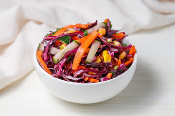 Healthy fresh salad with red cabbage, cucumber, carrot and corn in a bowl on white wooden table. Bright vegetarian food close up