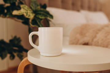 White coffee cup on the table in sunny morning bedroom, mock up.