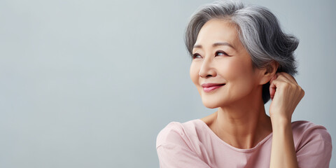 Happy Asian Woman. Portrait of Beautiful Older Mid Aged Mature Smiling Woman in Pink Clothes Isolated on Grey Background. Anti-aging Skin Care Face Beauty Product. Banner with Copy Space.