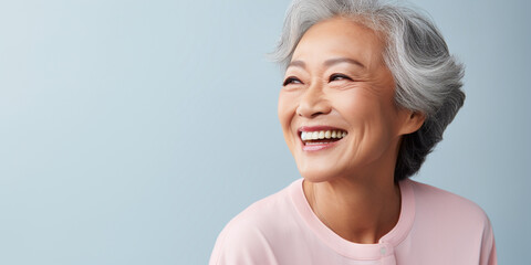 Happy Asian Woman. Portrait of Beautiful Older Mid Aged Mature Smiling Woman in Pink Clothes Isolated on Grey Background. Anti-aging Skin Care Face Beauty Product. Banner with Copy Space.