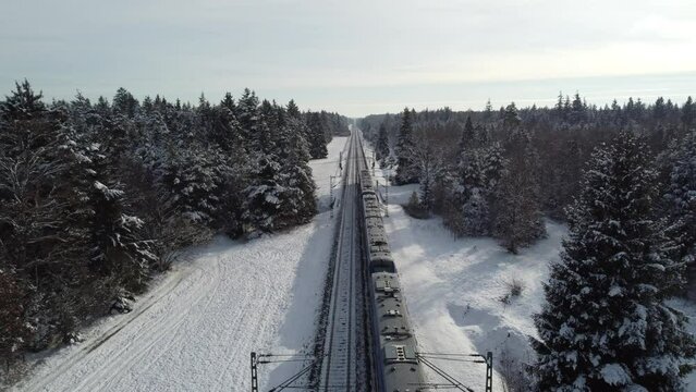 Top aerial view of regional train train driving on track rails crossing through snowy forest in winter near Munich