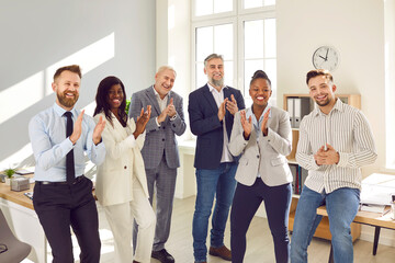 Happy diverse business team clapping hands together. Group of joyful multiethnic people standing in office, applauding and smiling. Work recognition, success, appreciation concept
