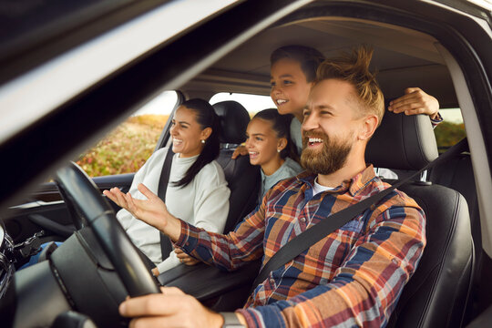 Portrait of happy laughing smiling family of four with children riding in modern car traveling by automobile together enjoying vacation or road trip on weekend. Family travel concept.