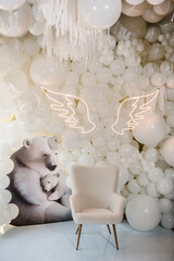 Reception at birthday baby party on wall. Arch decorated white balloons, angel wings, bears and chair for baptism. Photo area decoration space with white background. Trendy decor. Celebration concept.