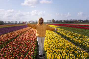 A young woman in a yellow jacket opened her arms to a field with colorful tulips
