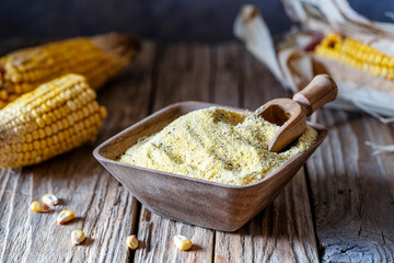 Corn flour or polenta wholemeal in a wooden bowl with small scoop, maize cobs over old wooden...