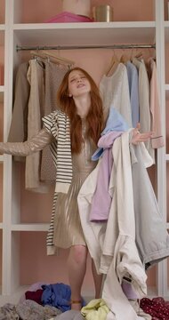 cheerful excited woman jumping with clothes happily in room at home, after shopping.caucasian redhead lady have fun, alone. a lot of clothes falls on her. people, human emotions, fashion concept