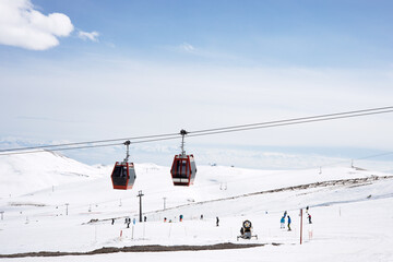Cable car or ski lift cabins moving against the background of snow-covered mountains and blue sky in the mountain ski resort. Perspective. Winter, Vacation. Extreme sport.  Travel content