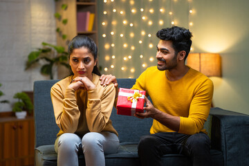 Angry indian girl rejecting gift from boyfriend while sitting on sofa at home during valentines day...