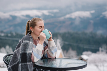 Female drink tea and relaxing on cabin terrace with mountain view. Woman sitting and holding cup...