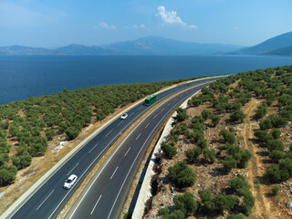 Beautiful view from a drone on an asphalt highway with cars among the trees on a sunny day near Lake Bafa, Turkey. Beautiful landscape with a road among mountains, trees and a lake.