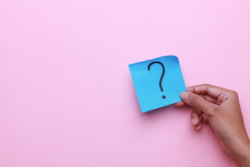 Hand holding sticky note with question marks symbol on pink background