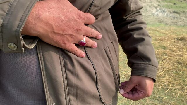 A person unzipping jacket pocket. Close up view of opening the zipper of the Brown jacket pocket. 