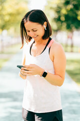 Vertical image of cheerful sport woman checking smatphone after morning run.