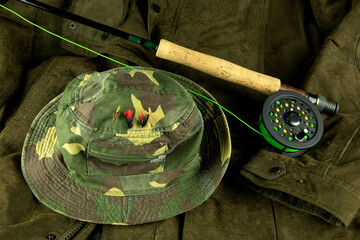 Fly Fishing Rod and Reel with Line on an Outdoor Coat with Fishing Hat and Trout Flies - 688595617