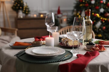 Christmas table setting with burning candles, appetizers and dishware indoors
