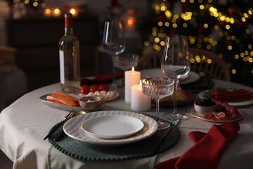 Christmas table setting with burning candles, appetizers and dishware indoors
