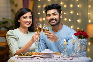 Happy smiling couple champagne wine in hands by looking at camera during candle light dinner at...