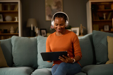 Obraz premium Woman with headphones using tablet computer while relaxing at home