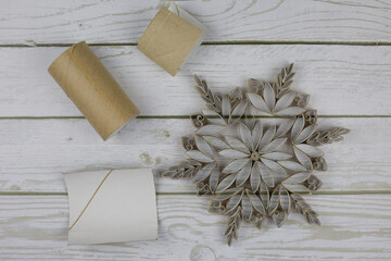 Craft a snowflake from toilet paper rolls. New Year's homemade toys from scrap materials. Home holiday decorations made from recycled materials on white wooden background