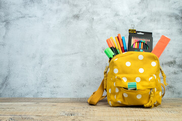 Backpack with different colorful stationery on table. Grey concrete background. Back to school