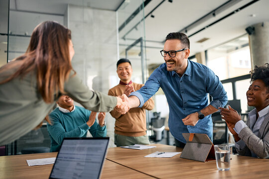 Happy businessman handshaking with female colleague during meeting in office while others are applauding.