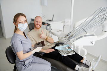 Portrait of young female dentist standing by mid adult man in clinic. Female dentist repairing patient tooth in dental ambulant