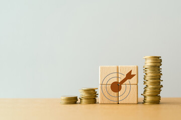 dartboard icon on wooden cube block and stack of coins including copy space for financial concepts...
