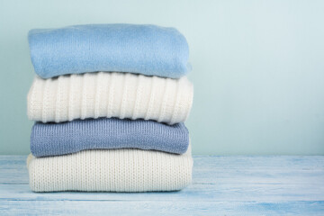 Knitted wool sweaters. Pile of knitted winter, autumn clothes on green, wooden background, sweaters, knitwear, space for text.
