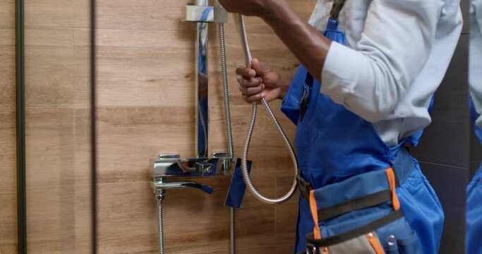 skilled black professional plumber in blue overalls uniform working in bathroom, plumbing repair service, assemble and install concept. hardworking plumber use tools and equipment in bathroom.