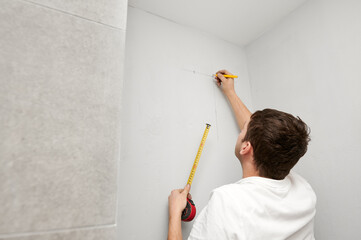 Male worker using tape measure and pencil while checking wall level before repair works. Man...