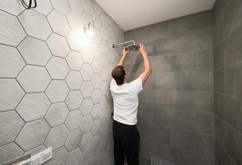 Back view of man standing by the wall with ceramic tile and installing high pressure bath...