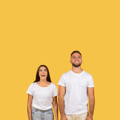 Obraz premium Happy shocked millennial european couple in white t-shirts, look up at empty space