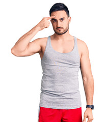 Young handsome man wearing swimwear and sleeveless t-shirt pointing unhappy to pimple on forehead, ugly infection of blackhead. acne and skin problem