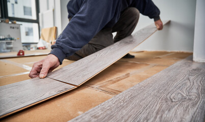 Close up of man hands laying laminate wooden planks on the floor in apartment under renovation....