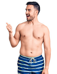 Fototapeta premium Young handsome man wearing swimwear smiling with happy face looking and pointing to the side with thumb up.