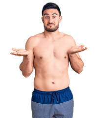Fototapeta premium Young handsome man wearing swimwear clueless and confused expression with arms and hands raised. doubt concept.