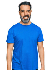 Middle aged man with beard wearing casual blue t shirt winking looking at the camera with sexy expression, cheerful and happy face.