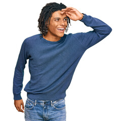 Young african american man wearing casual winter sweater very happy and smiling looking far away with hand over head. searching concept.