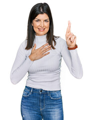 Beautiful brunette woman wearing casual clothes smiling swearing with hand on chest and fingers up,...