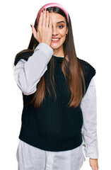 Young beautiful woman wearing casual white shirt covering one eye with hand, confident smile on face and surprise emotion.