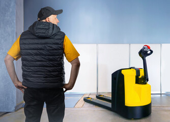 Man near electric pallet jack. Warehouse worker with back to camera. Pallet jack for loading...