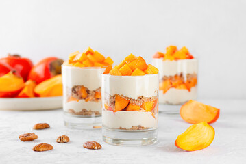 Parfait in a glasses with persimmon, pecan, whipped cream and biscuit. Healthy food, vegan, sugar, gluten and lactose free.