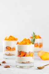 Parfait in a glasses with persimmon, rosemary, pecan, whipped cream and biscuit. Healthy food,...