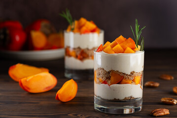 Dessert in a glasses with persimmon, rosemary, pecan, whipped cream and biscuit on a wooden table....