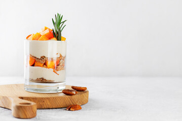 Dessert in a glass with persimmon, rosemary, pecan, whipped cream and biscuit. Healthy food, vegan,...