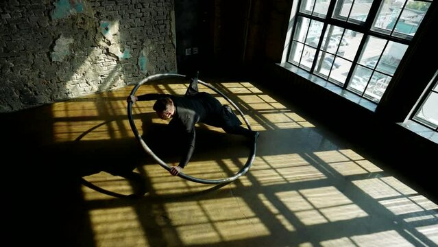 acrobat man dancing and performing trick with hoop in room, top view, slow-motion shot